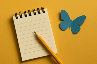 Caderno em uma mesa amarela com uma borboleta de papel.